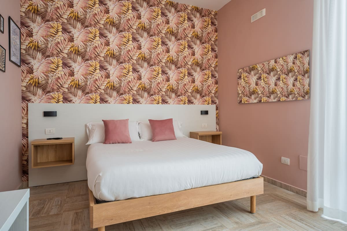 A bedroom with a large bed, two bedside tables, a wall-mounted artwork, and a patterned wallpaper.