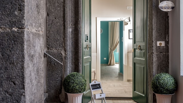 A hallway with two green doors, a welcome sign, and potted plants. - B&B Pontenuovo Bed (Naples)