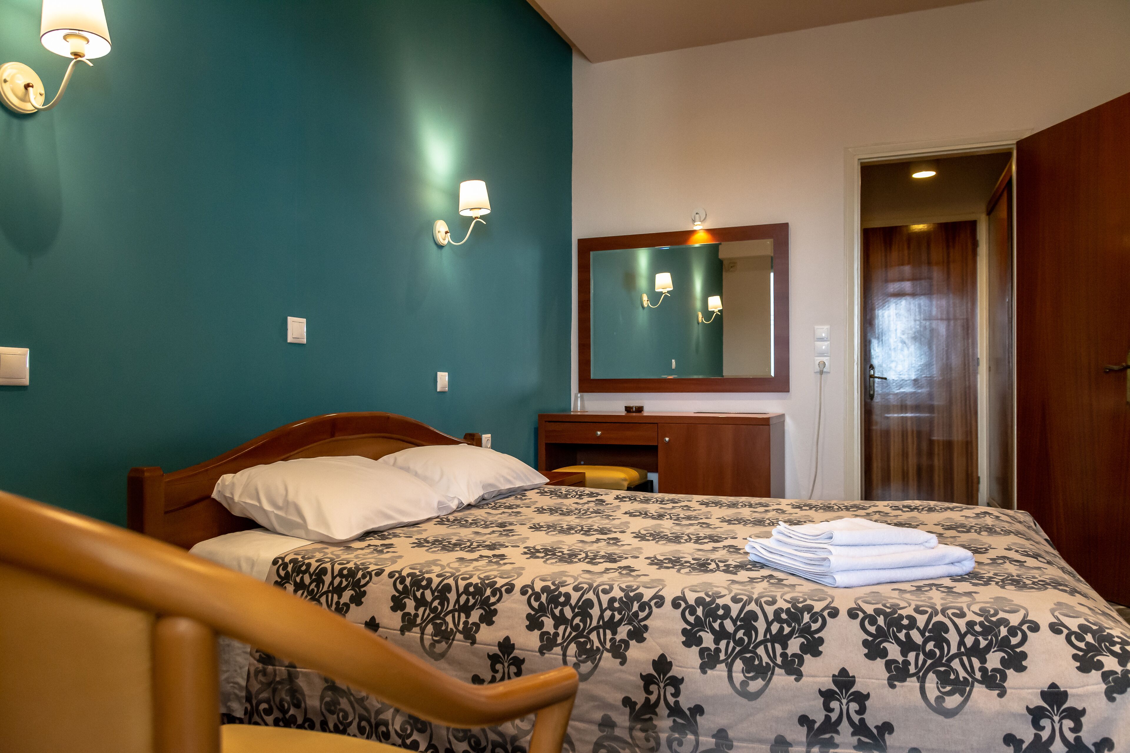 A neatly made bed with a patterned bedspread, a wooden nightstand with a lamp, and a mirror above the dresser.