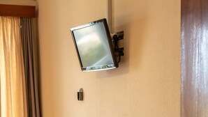 Une chambre d’hôtel avec un bureau en bois, une chaise, un téléviseur fixé au mur et une porte avec un radiateur.