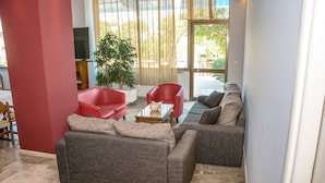Un salon comprenant un canapé, un fauteuil rouge, une table basse et un téléviseur.