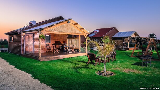 Een rustieke blokhut met houten gevel, een veranda met zitplaatsen buiten en een kleine tuin.