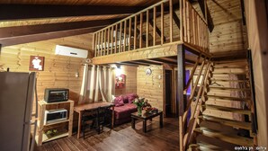 Een houten blokhut van binnen met een eethoek, een bank, een trap en een keuken met apparatuur.