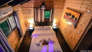 Een gezellig kamer in een blokhut met houten inrichting, een bed met handdoeken, een schilderij aan de muur en een raam met gordijnen.
