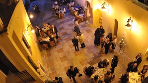 An outdoor dining area with multiple tables and chairs, surrounded by buildings with arches and columns. - Castello di Altomonte (Altomonte)