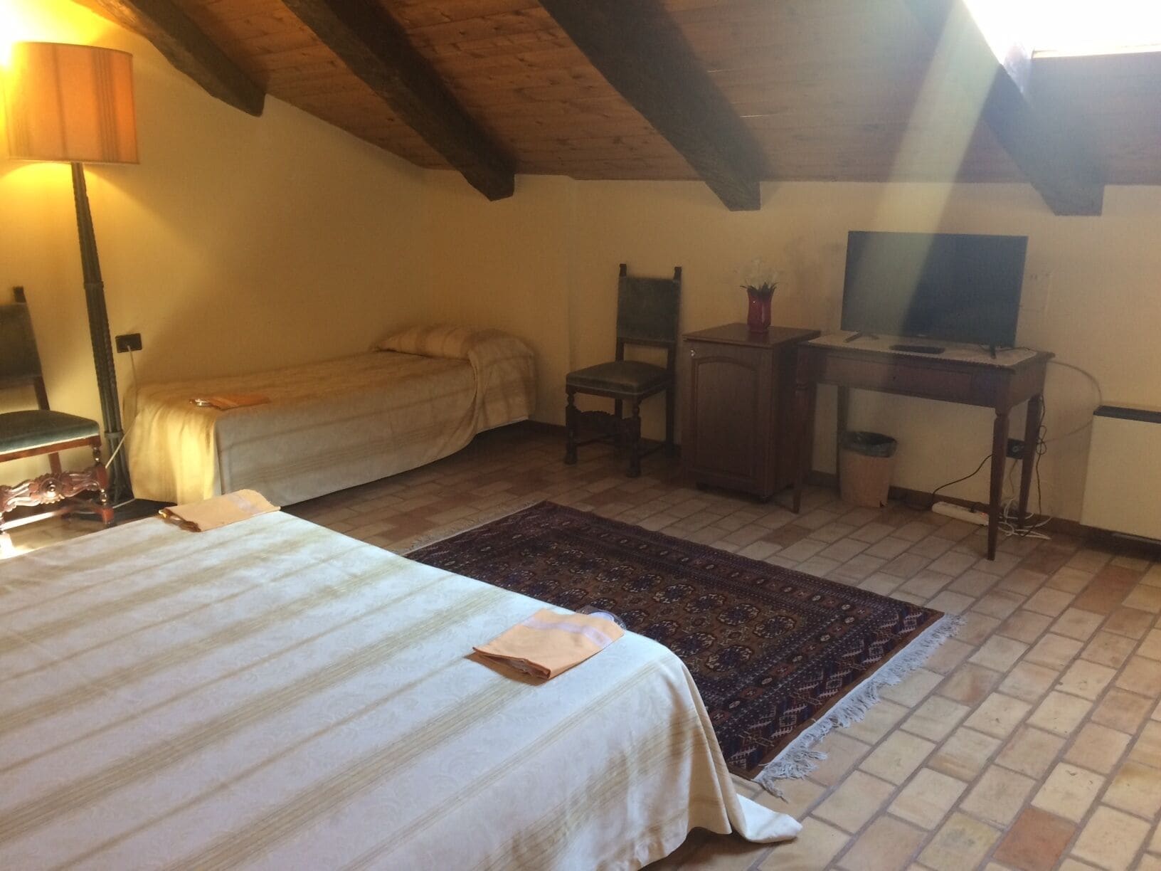 Un dormitorio con cama, escritorio, silla, televisor y lámpara.