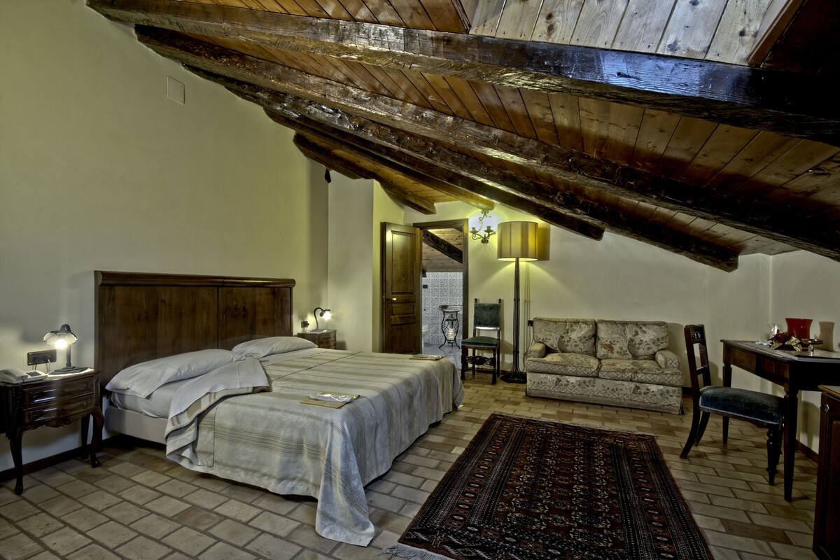 A bedroom with a wooden ceiling, a bed, a sofa, and a small table.