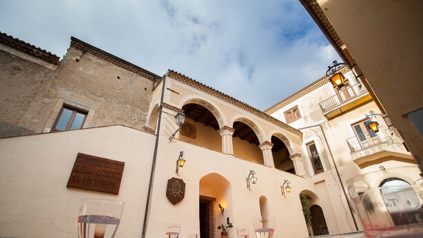 A building with a red carpet leading to a door, a sign reading "Il Castello dei Conti Albergro-Ristorante Sala Ricevimenti", and a balcony with a railing. - Castello di Altomonte (Altomonte)