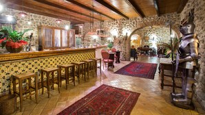 A rustic interior with stone walls, wooden beams, a bar area with stools, and a dining area with a large rug. - Castello di Altomonte (Altomonte)