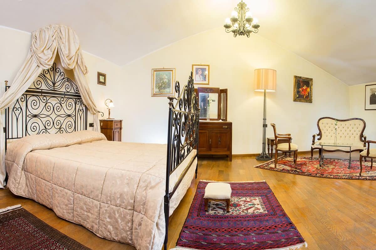 A bedroom with a four-poster bed, a wooden dresser, a desk, a chair, and a television.
