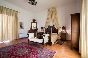 A bedroom with a four-poster bed, a sitting chair, a dresser, and a large red rug.