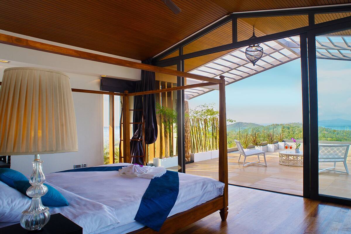A bedroom with a large bed, a bedside lamp, and a view of the outdoors through a glass door.