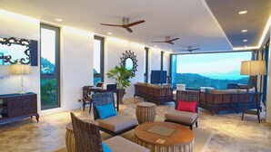 Un amplio salón con diversas opciones de asientos, un ventanal con vistas al exterior y ventiladores de techo.