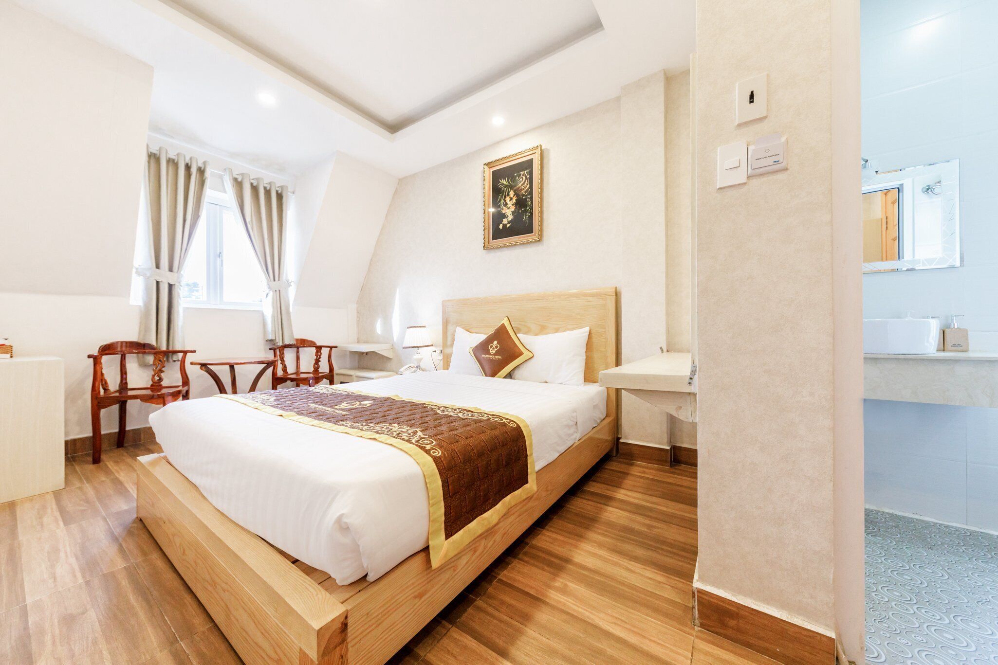 Hotelkamer met een groot bed, houten hoofdbord, nachtkastje, stoel, bureau en een zichtbare badkamer door een open deur.