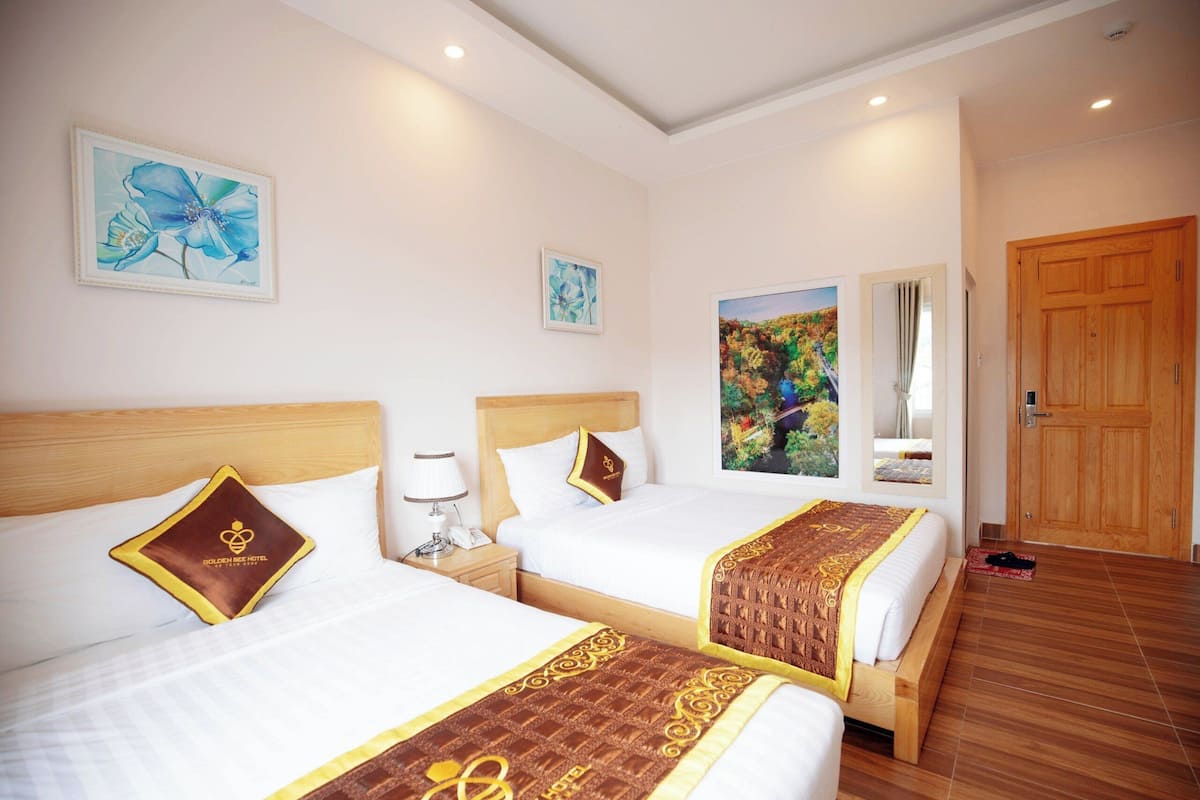 A hotel room with two beds, wooden headboards, white bedding, and artwork on the walls.