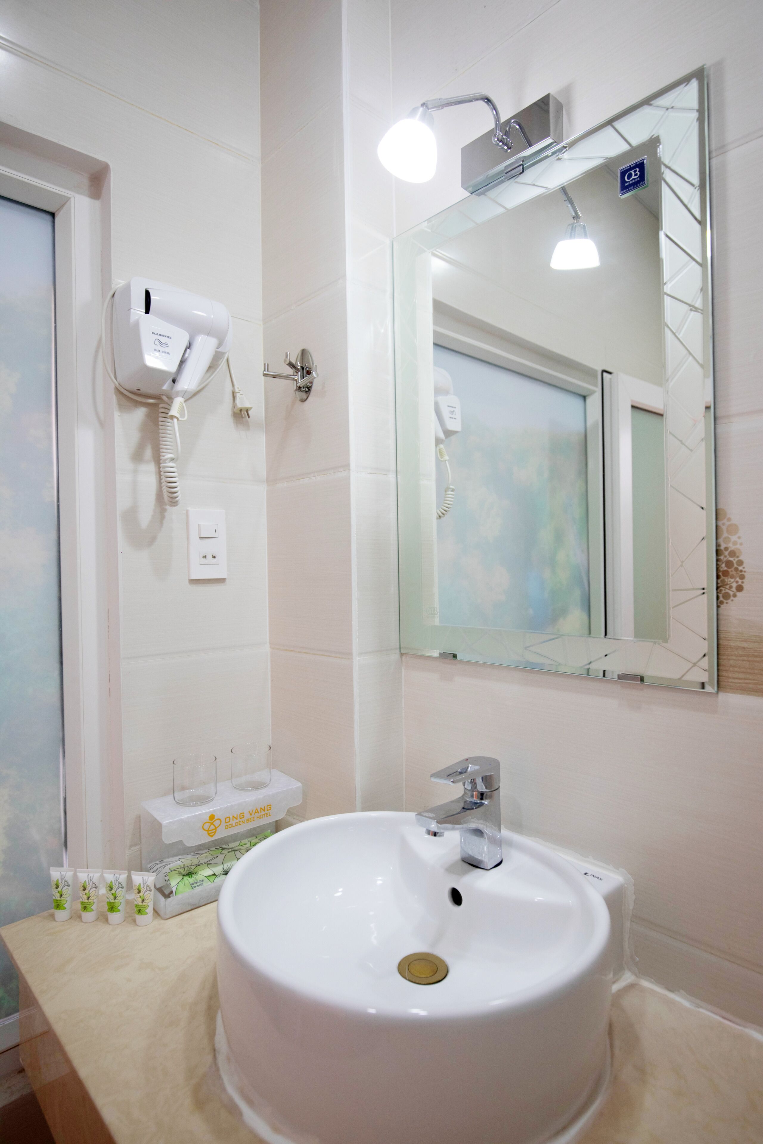 Een badkamer met een witte wastafel, een spiegel en een haardroger bevestigd aan de muur.