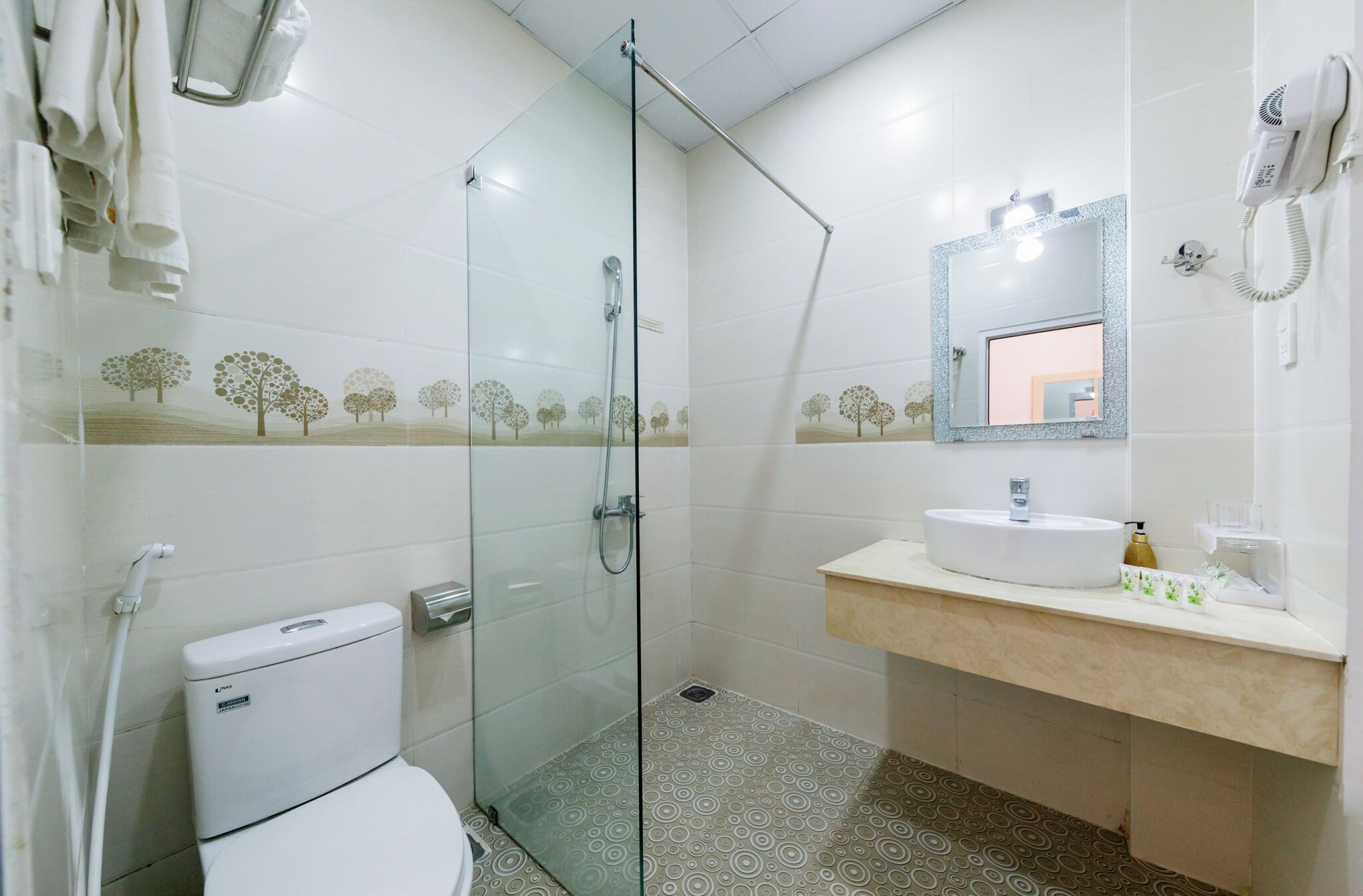 Bagno con toilette, lavabo con specchio, asciugacapelli e doccia con porta in vetro.