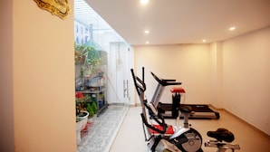 Een hotelgymzaal met fitnessapparatuur, een glazen wand met planten en een bord dat het fitnessgebied aangeeft.