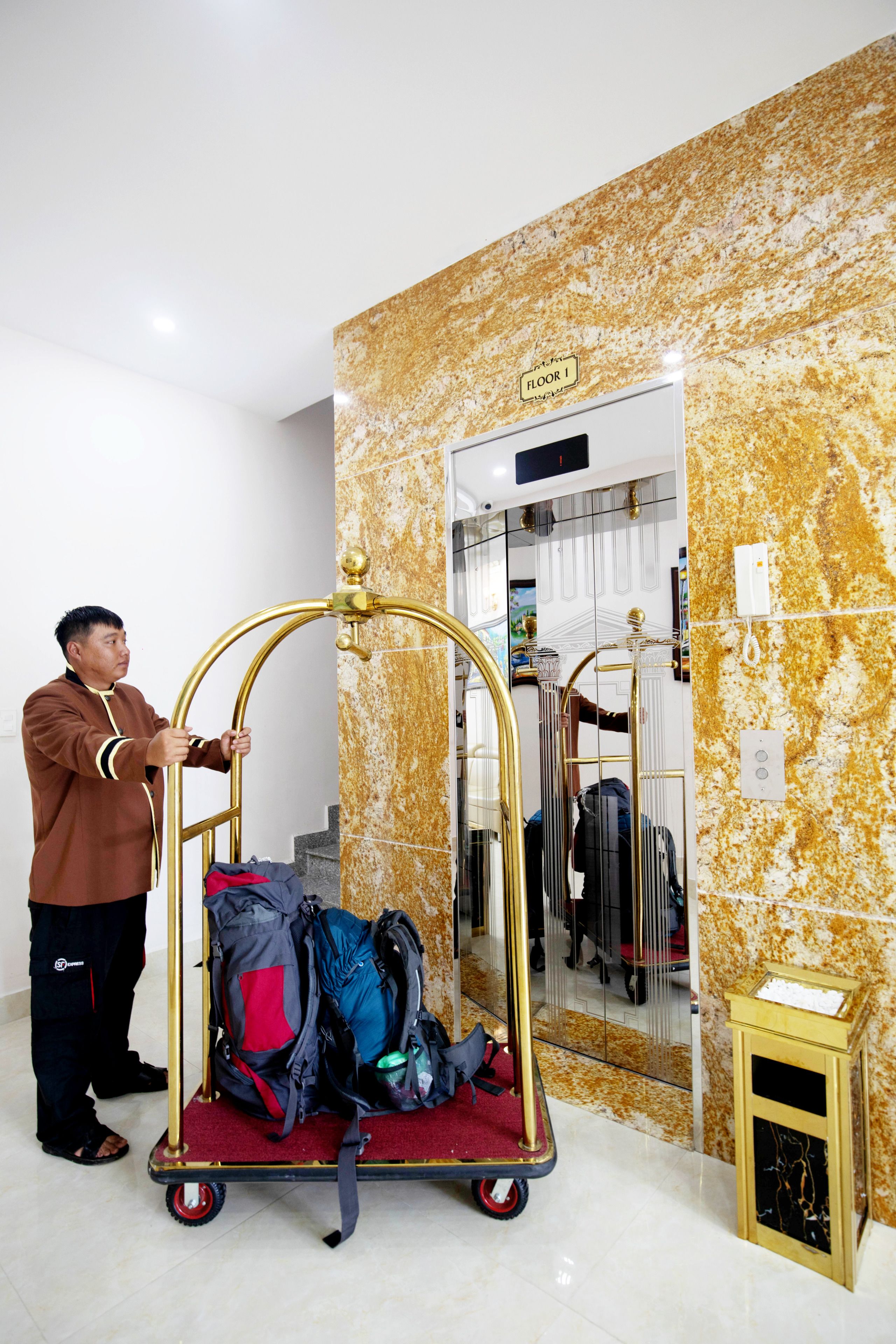 A man pushing a luggage cart with multiple bags in a hotel lobby with a marble wall and a sign indicating 'Floor 1'.