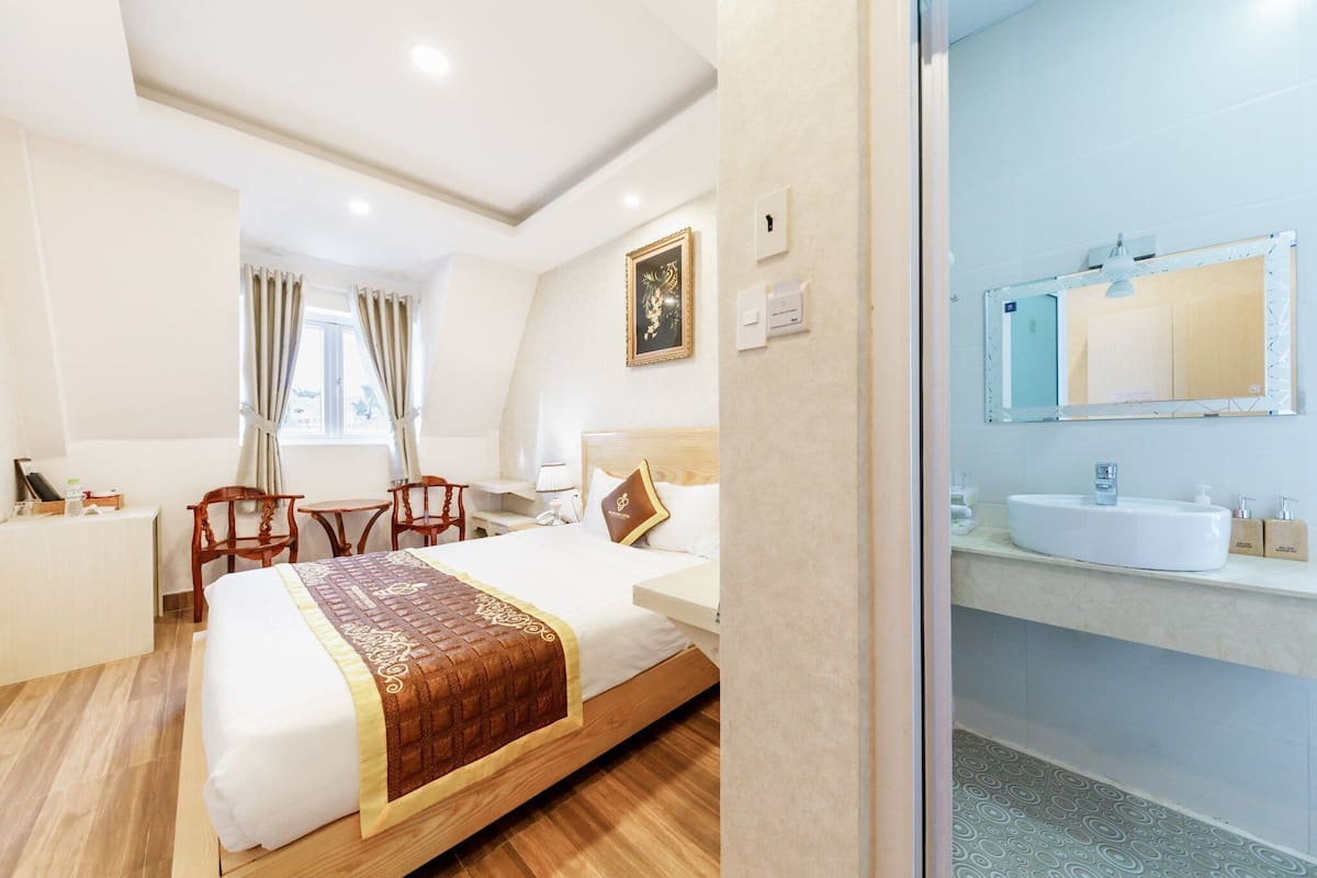 A hotel room with a bed, bedside table, chair, and a bathroom with a sink and mirror.