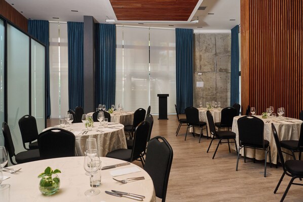 Un comedor con mesas redondas, sillas negras y cortinas azules.