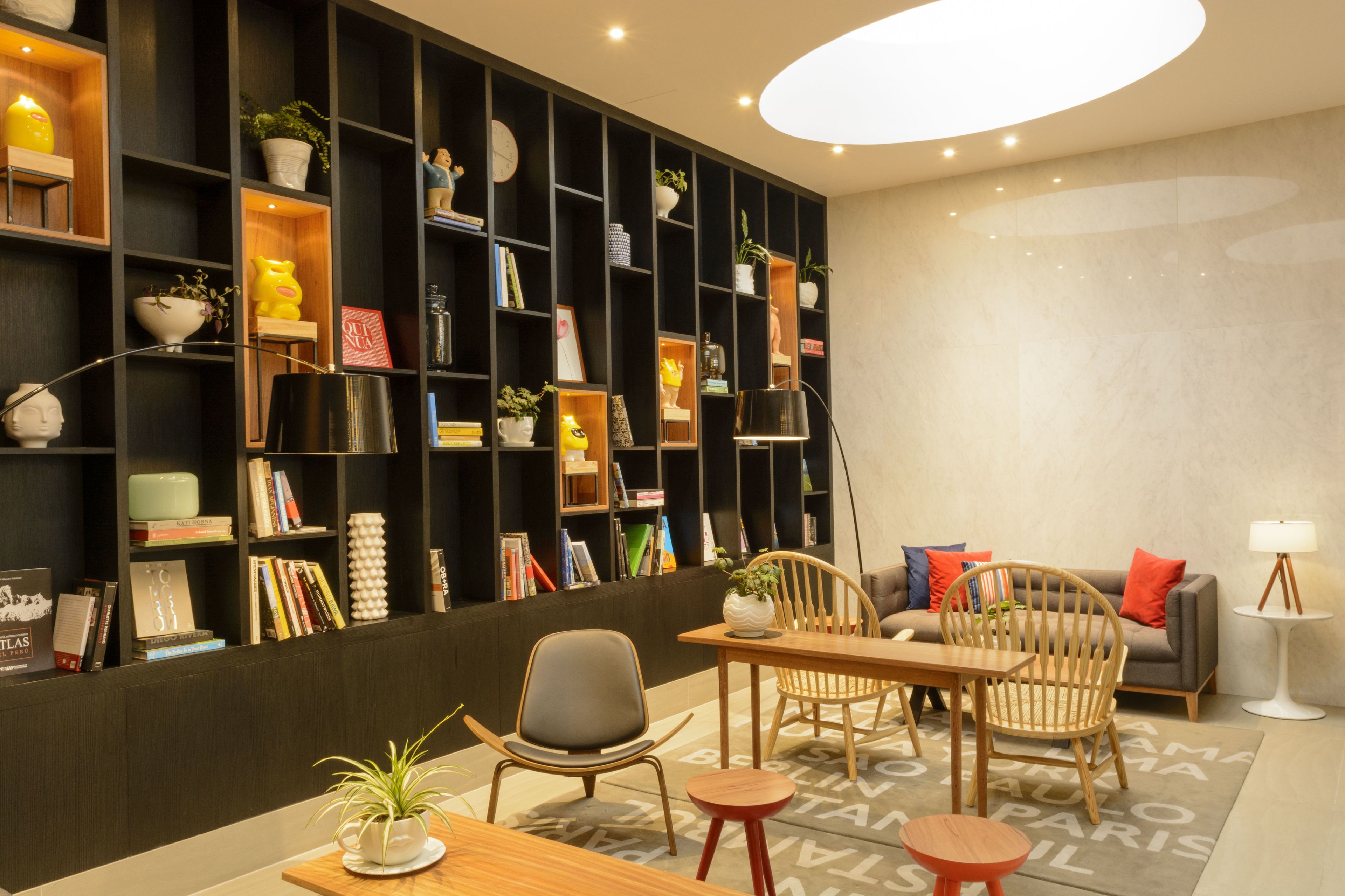 A modern interior with a wooden dining table, chairs, a sofa, and a bookshelf filled with books and decorative items.
