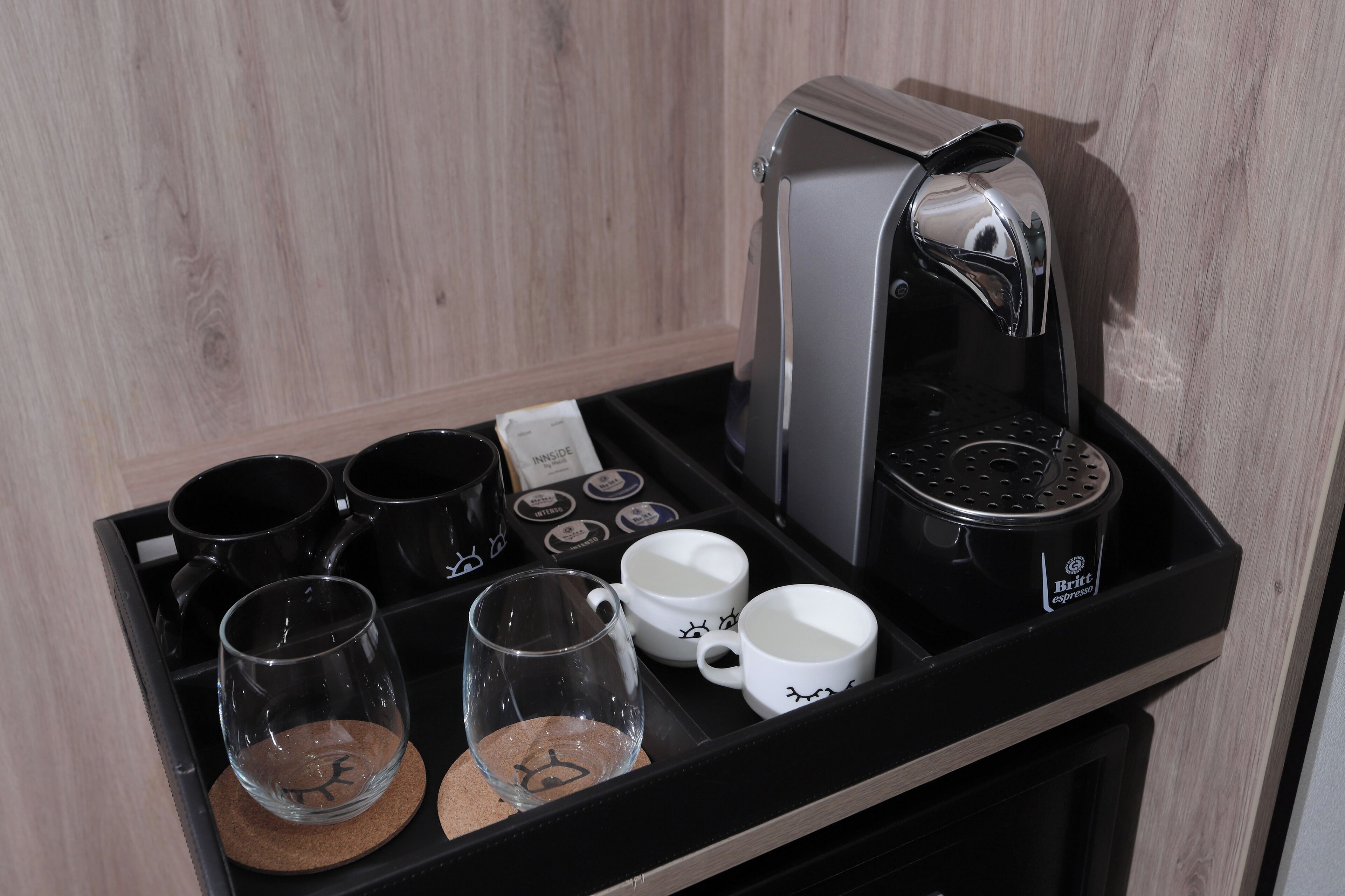 A coffee station with a coffee maker, cups, and a tray.