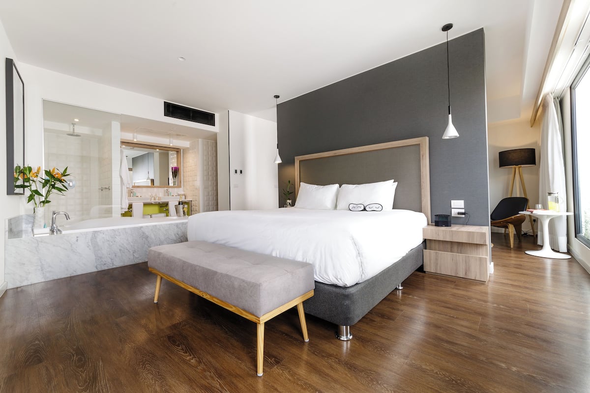 Quarto moderno com uma cama grande, um banco, uma mesa de cabeceira e um espelho.
