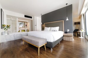 A modern bedroom with a large bed, a bench, a bedside table, and a mirror.