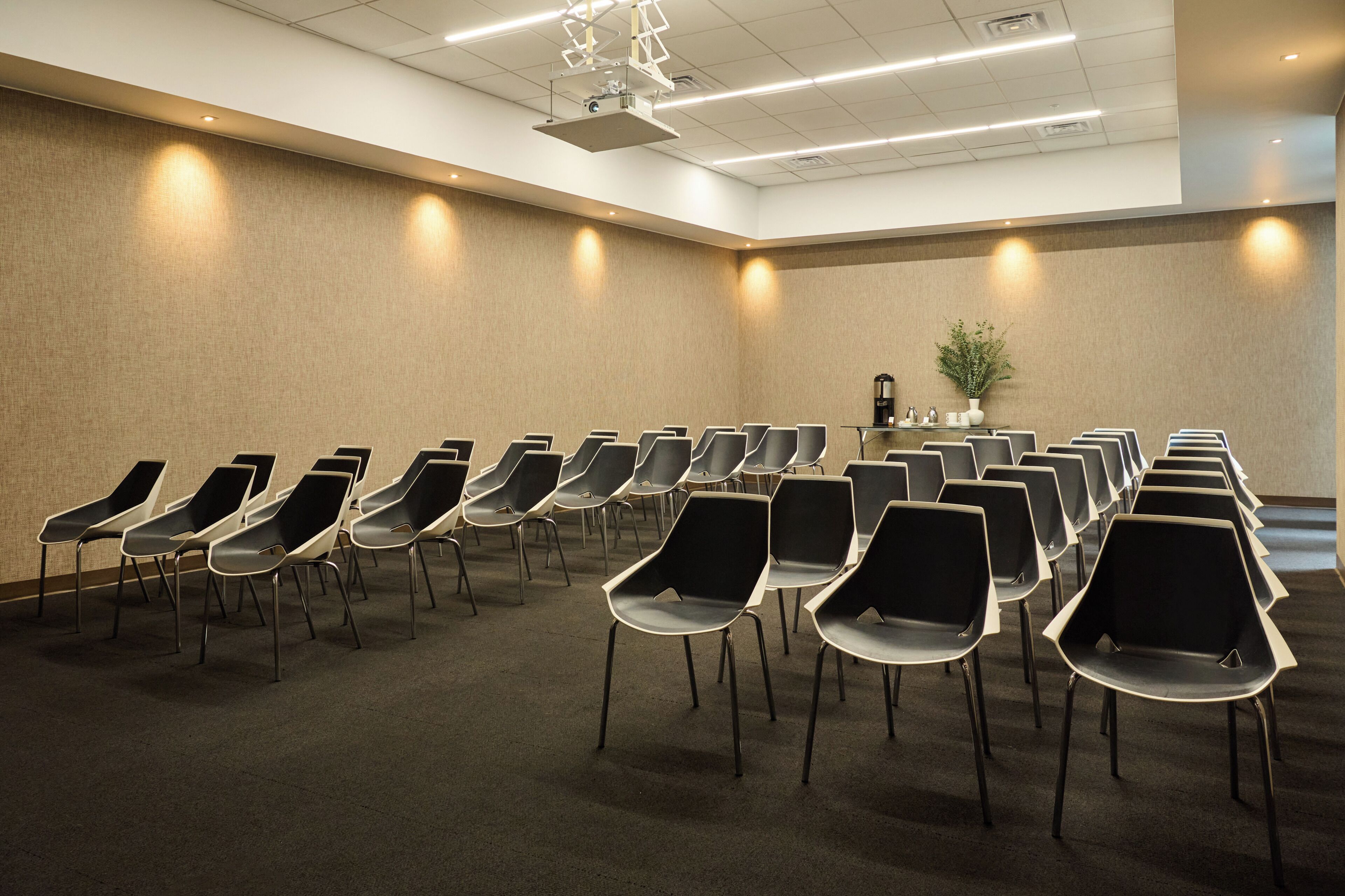 A conference room with rows of chairs, a podium, and a projector on the ceiling.