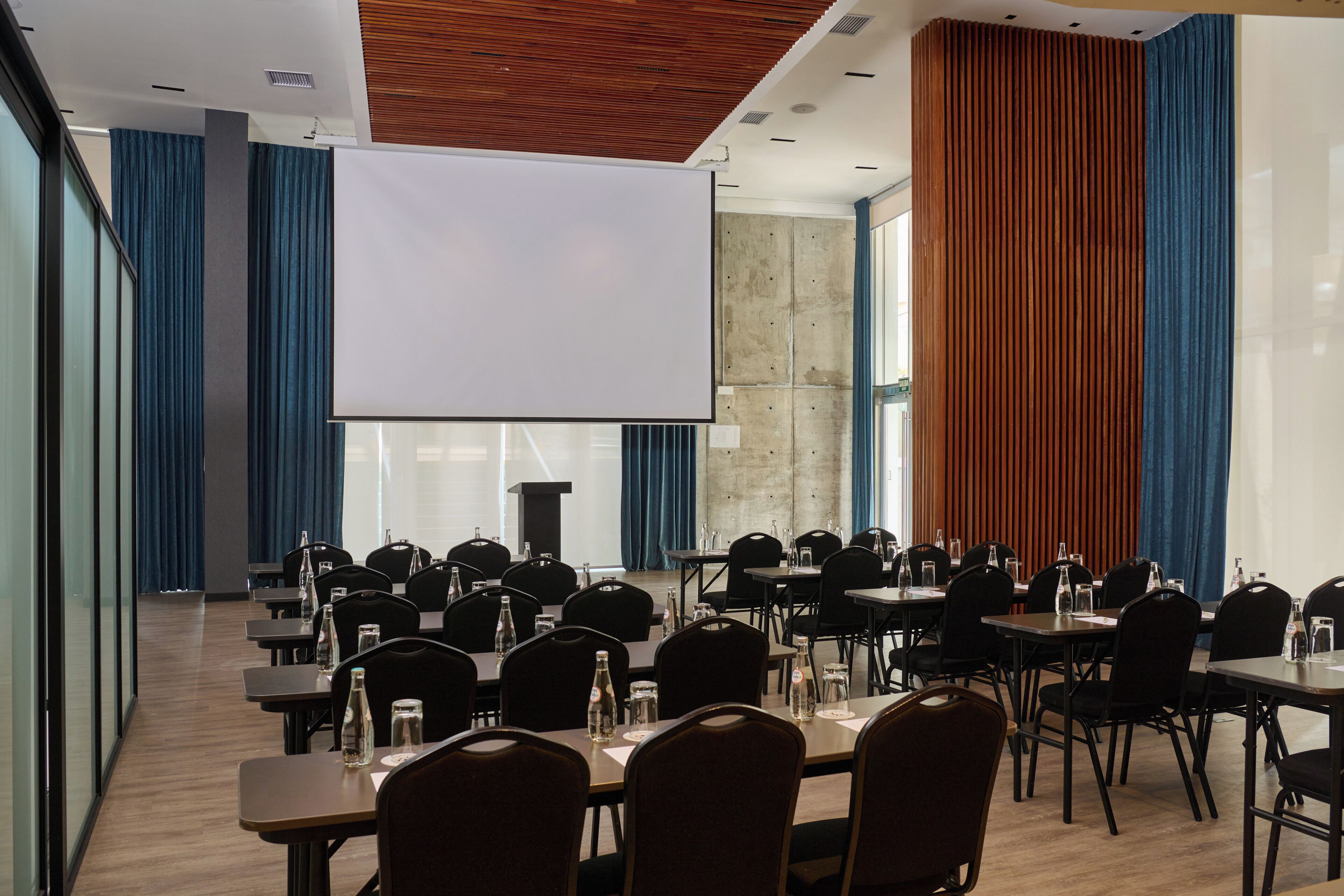 A conference room with tables, chairs, and a large screen.