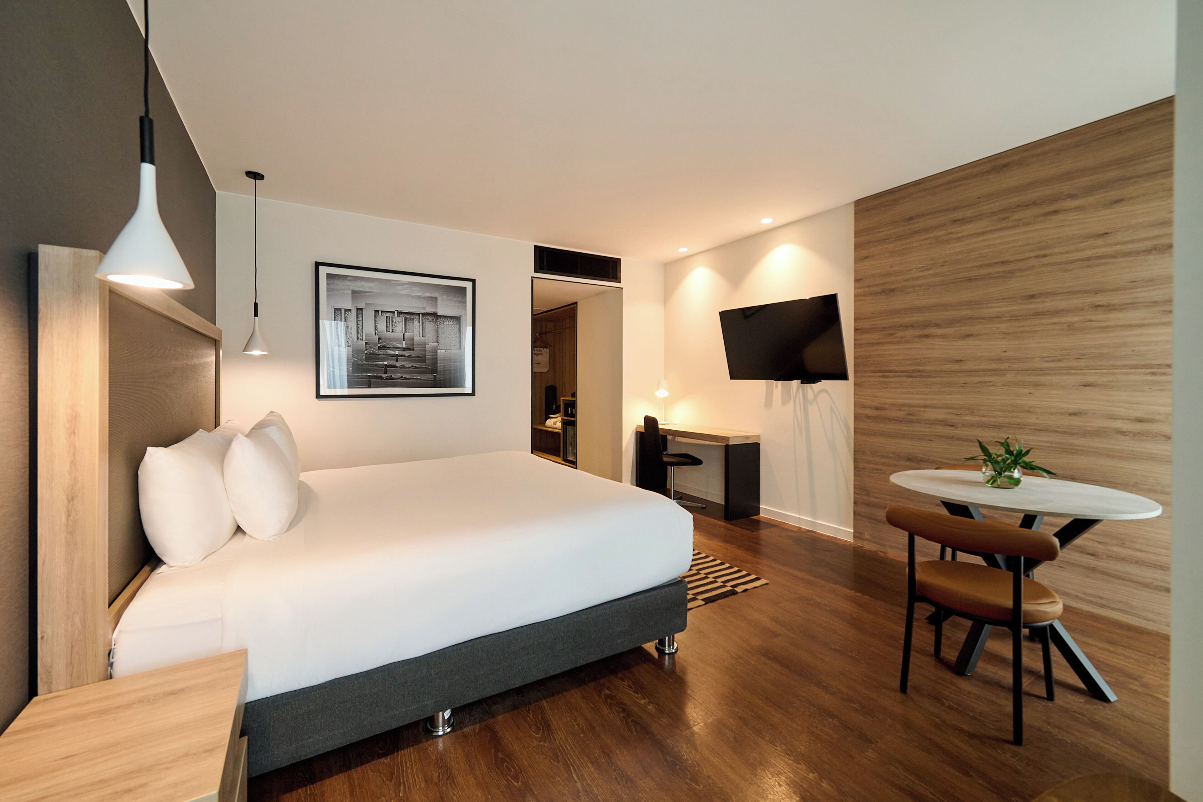 A modern hotel room with a large bed, a desk, a chair, a TV, and a small table with a plant.
