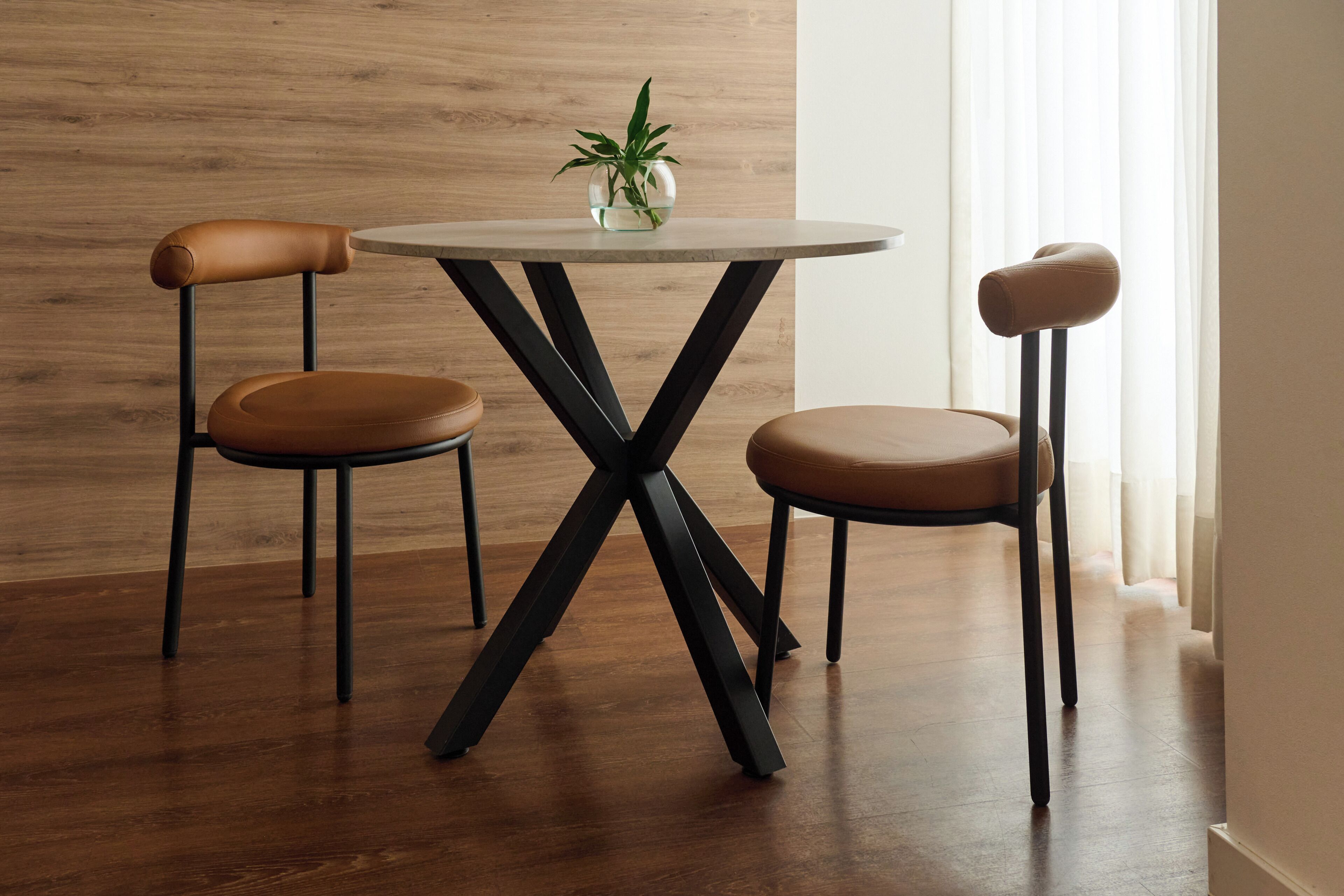 A dining area with a round table, two chairs, and a potted plant.