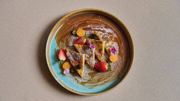 A plate with triangular food items, possibly pancakes, topped with strawberries, blueberries, and orange slices, and a dusting of powdered sugar.