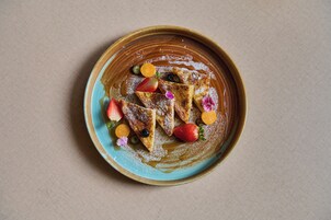 A plate with triangular food items, possibly pancakes, topped with strawberries, blueberries, and orange slices, and a dusting of powdered sugar.