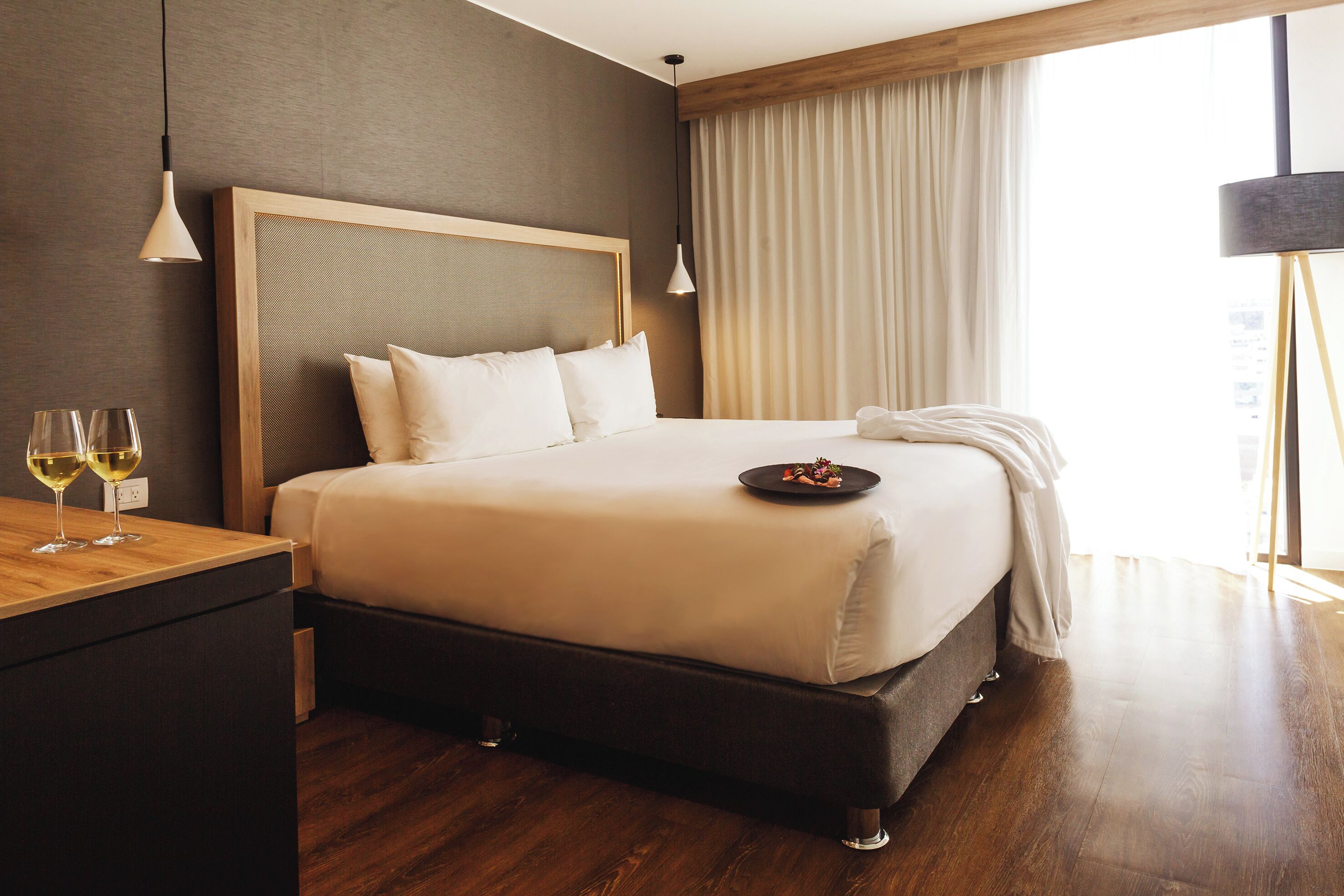 A hotel room with a large bed, bedside table, and a window with curtains.