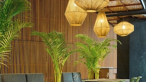 A restaurant with bamboo walls, green chairs, and hanging bamboo lamps.