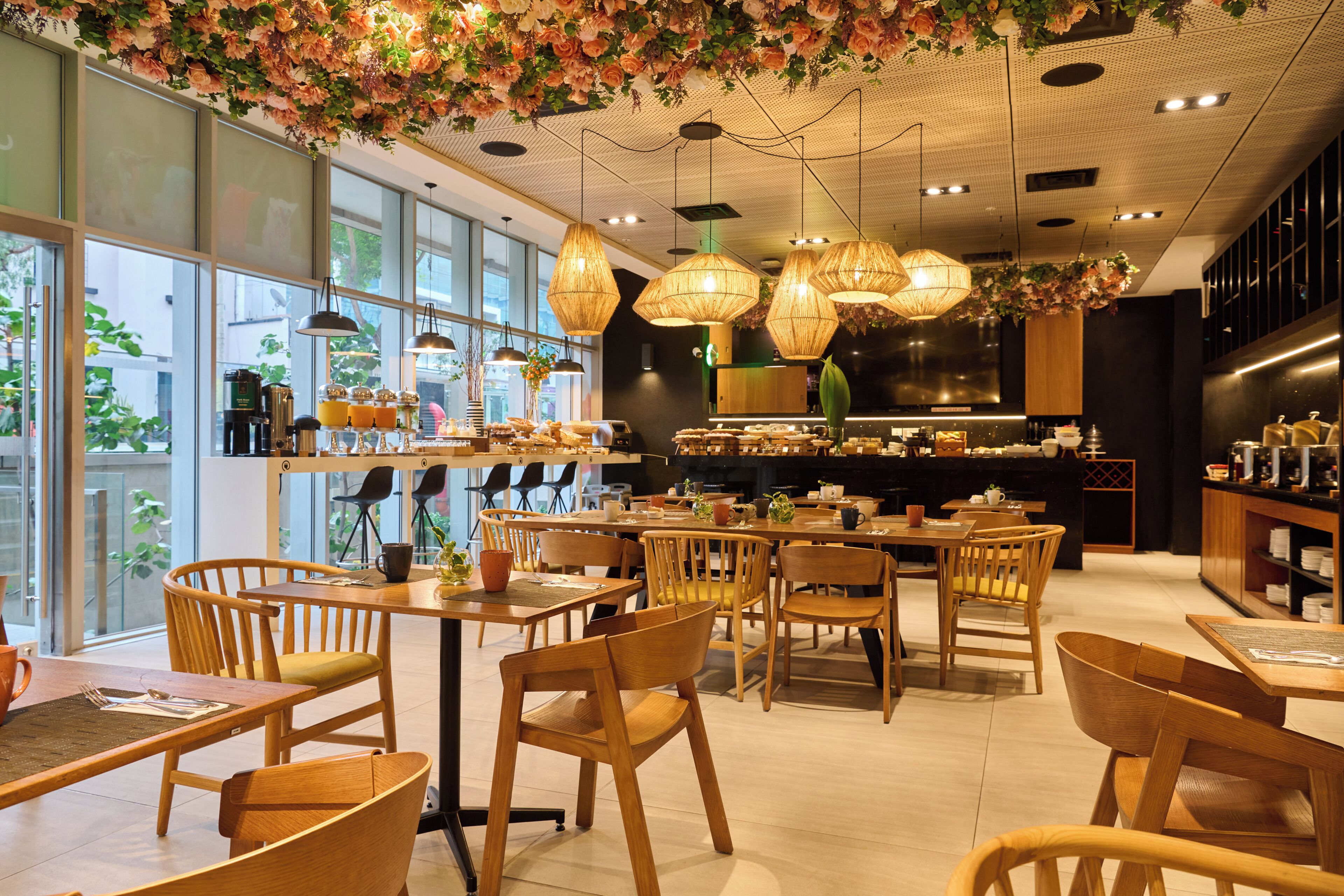 Una cafetería moderna con mobiliario de madera, ventanas amplias y decoraciones florales colgantes.