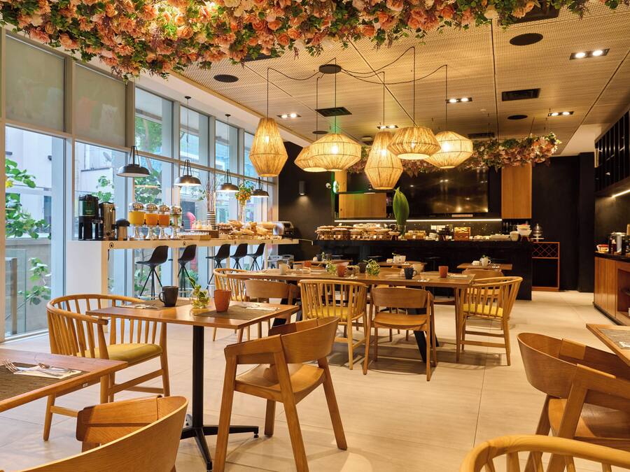 A modern cafe with wooden furniture, large windows, and hanging floral decorations.