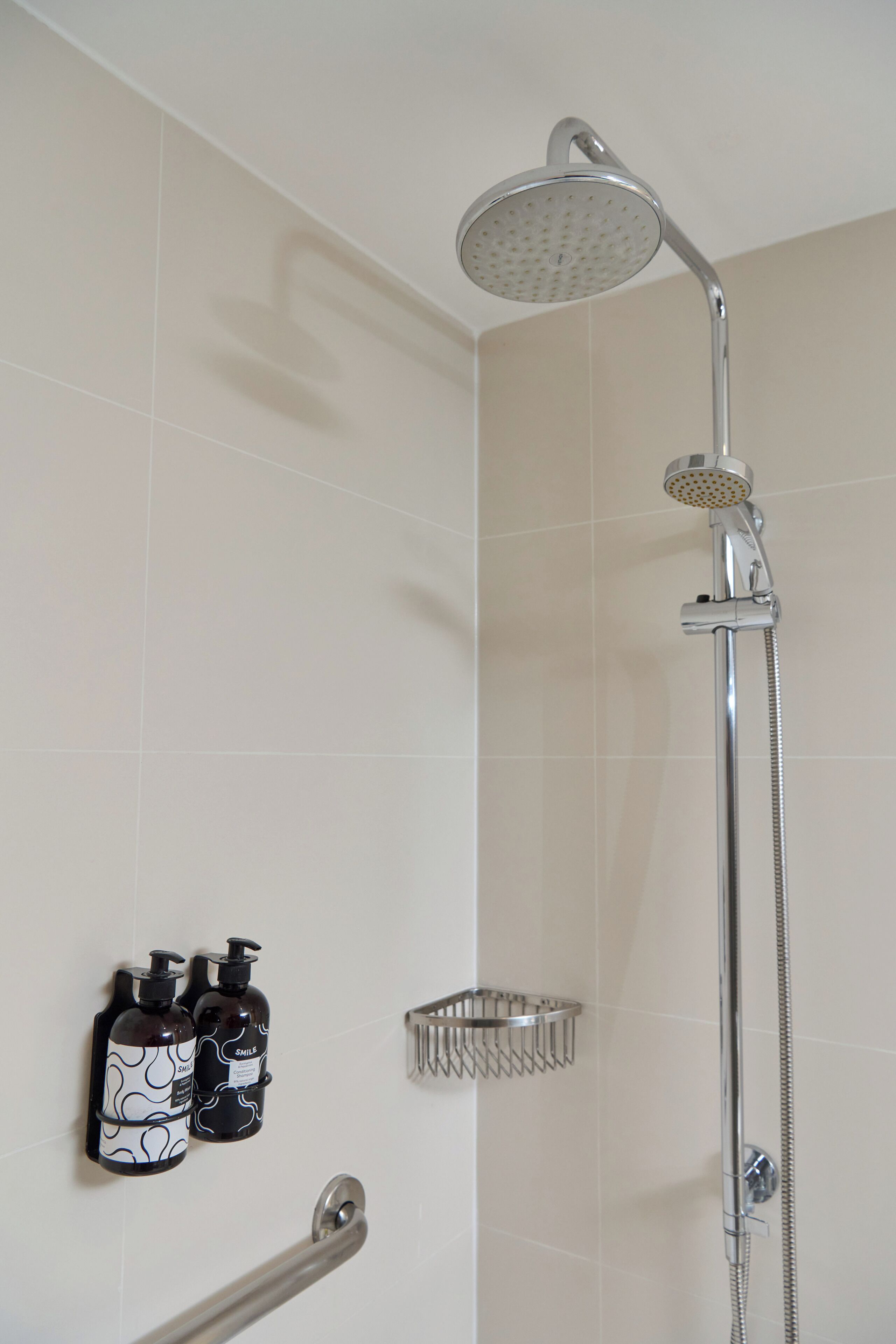 A shower with a handheld showerhead and a wall-mounted faucet. There are two soap dispensers on the wall.