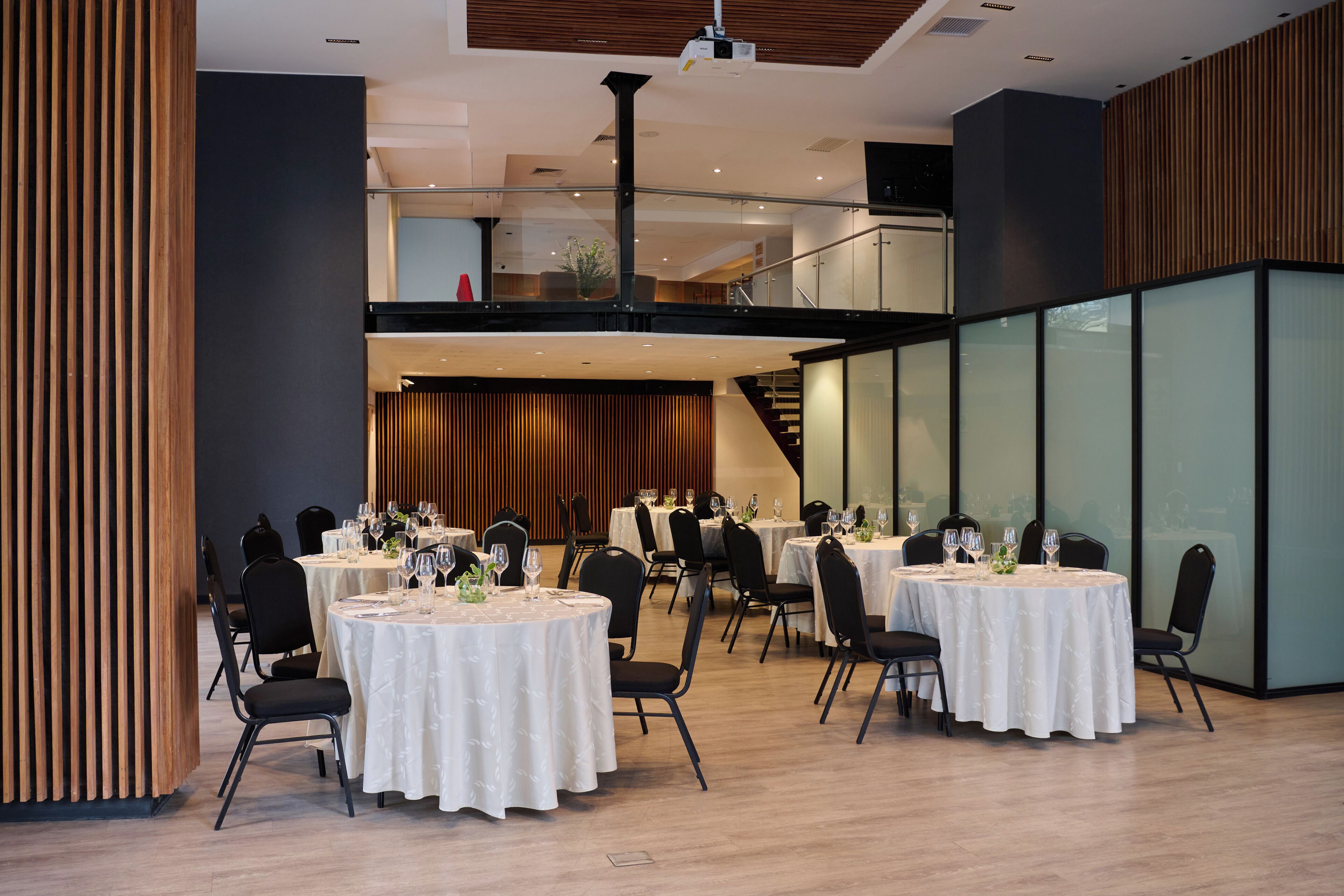 Un comedor moderno con mesas redondas, sillas negras y una pared de acento de madera.