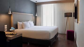 Une chambre d’hôtel moderne avec un grand lit, un bureau avec une lampe, un lampadaire et un téléviseur fixé au mur.
