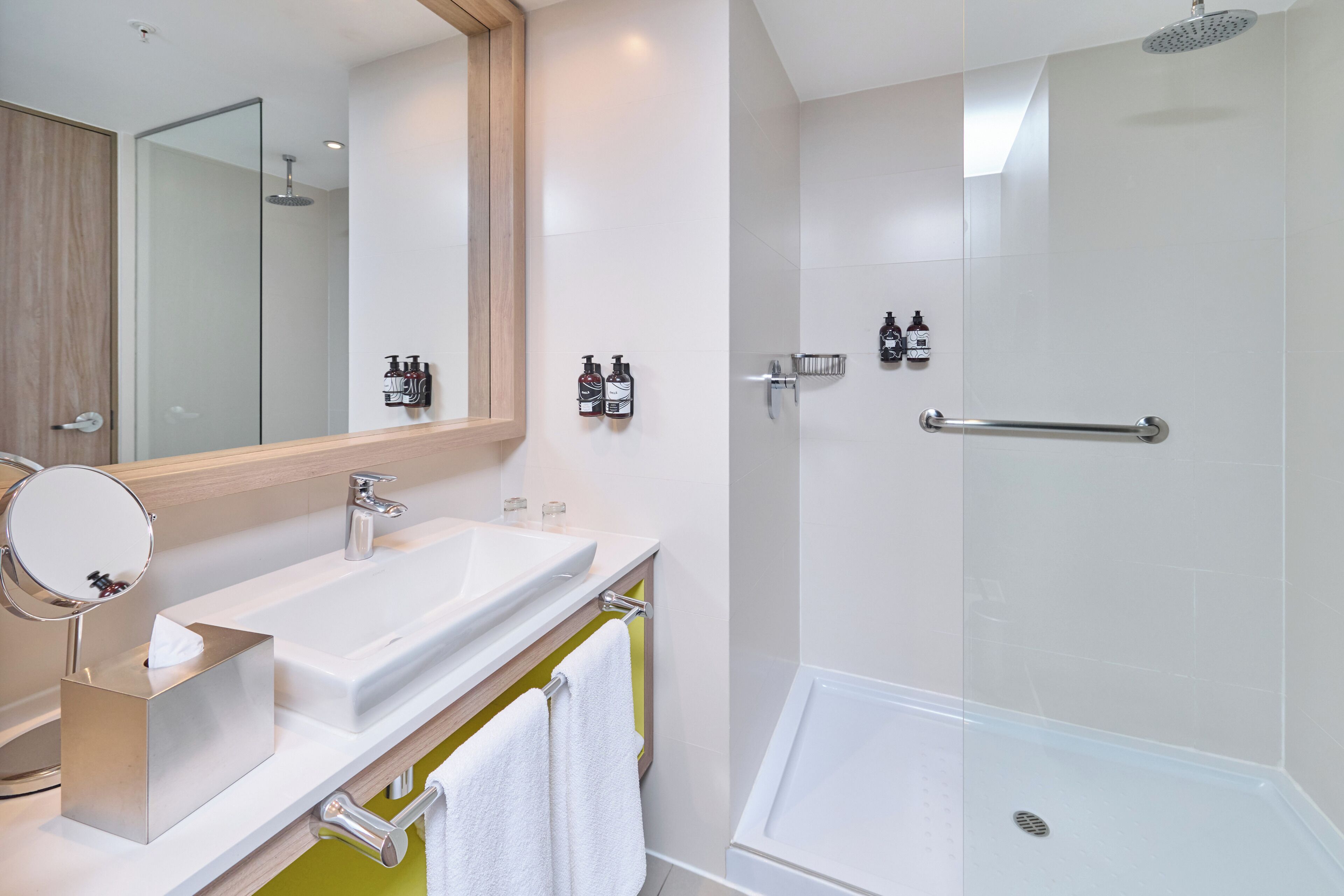 Un baño moderno con un espejo grande, dos lavamanos, una ducha y un perchero para toallas.
