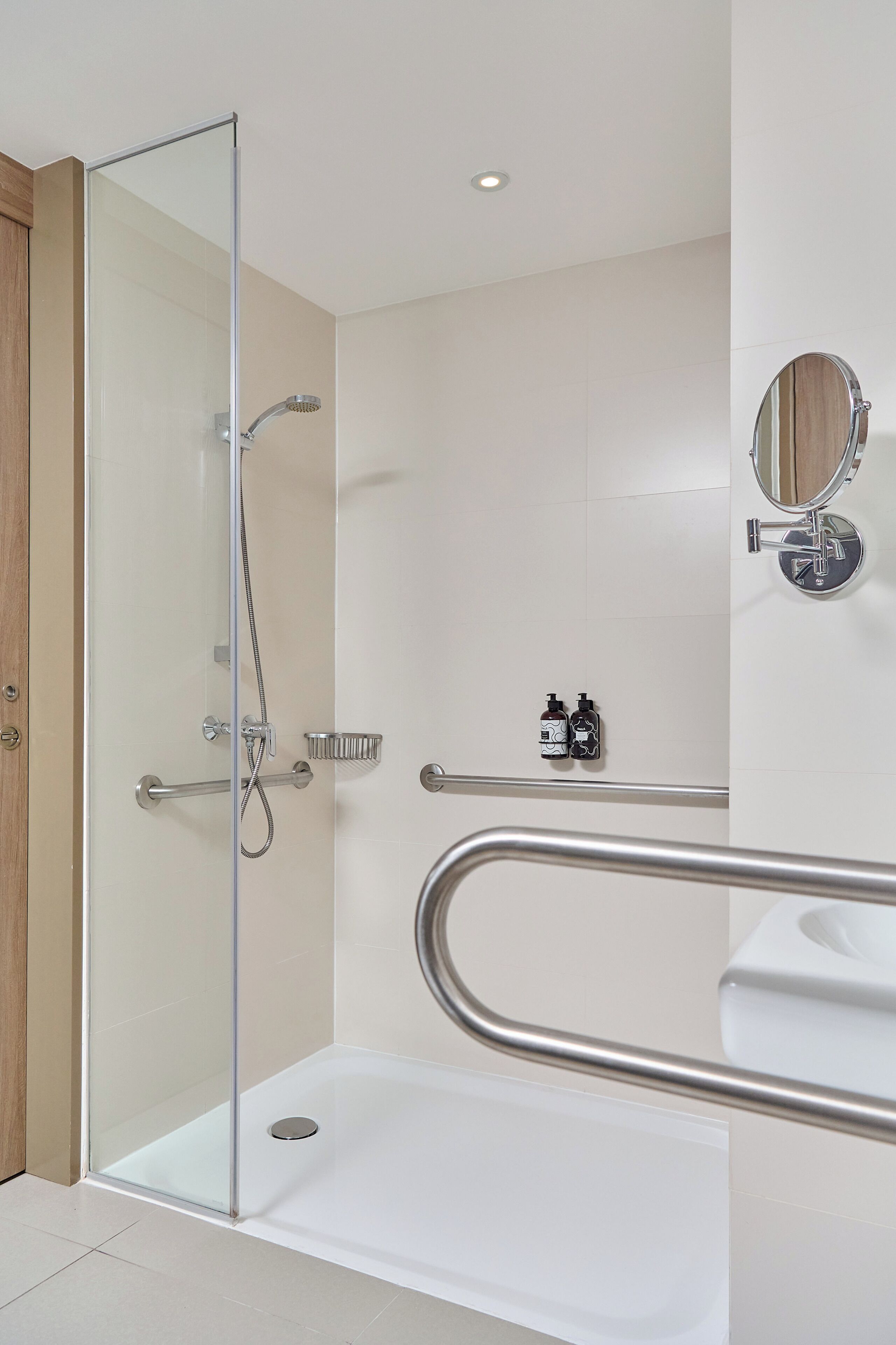 A modern bathroom with a glass-enclosed shower, a white sink, and a wooden door.