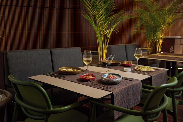 A dining table set with plates, glasses, and cutlery, surrounded by green chairs.