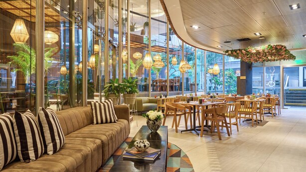 A modern hotel lobby with a sofa, dining area, and large windows.