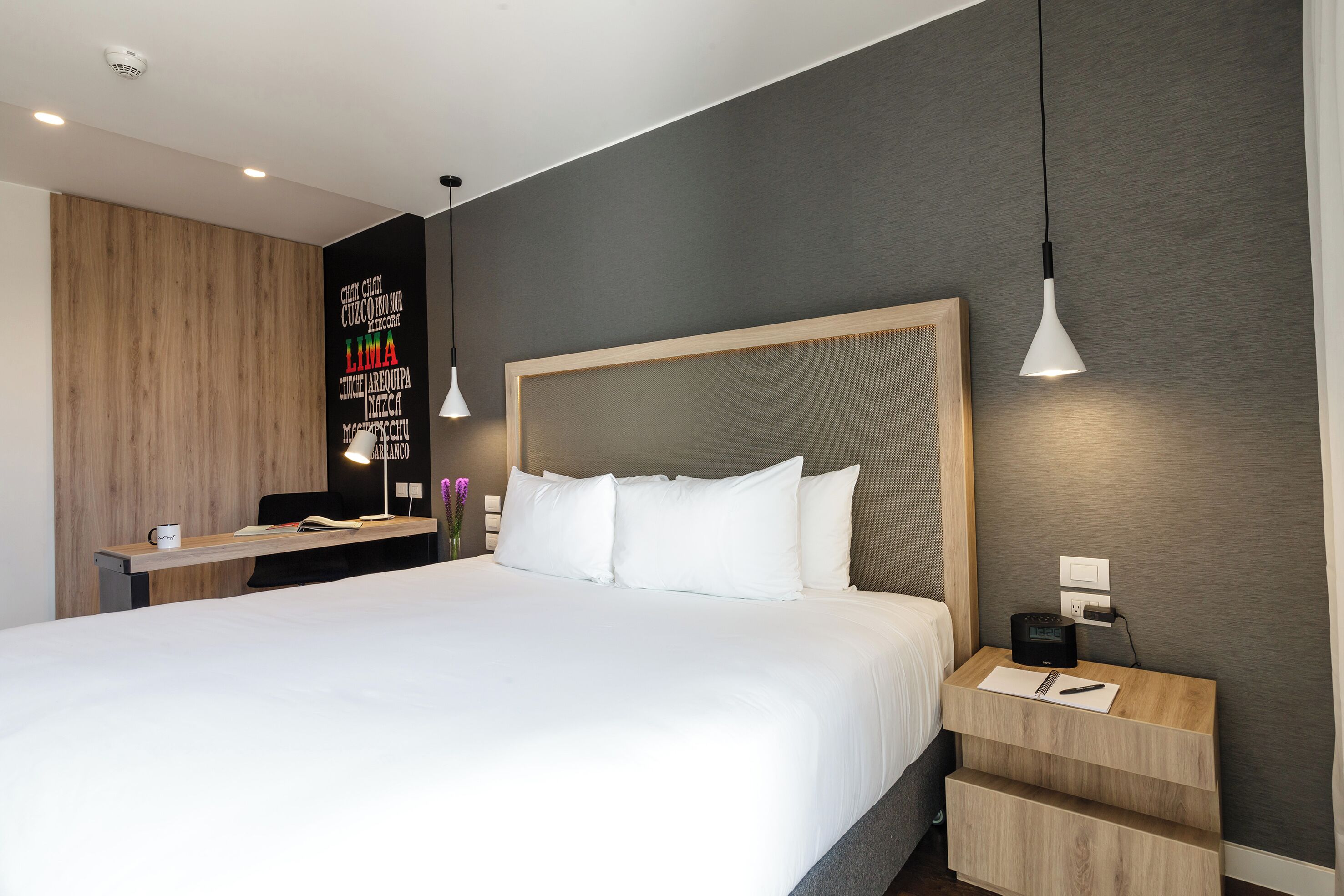 A modern hotel room with a large bed, a desk, and a nightstand.