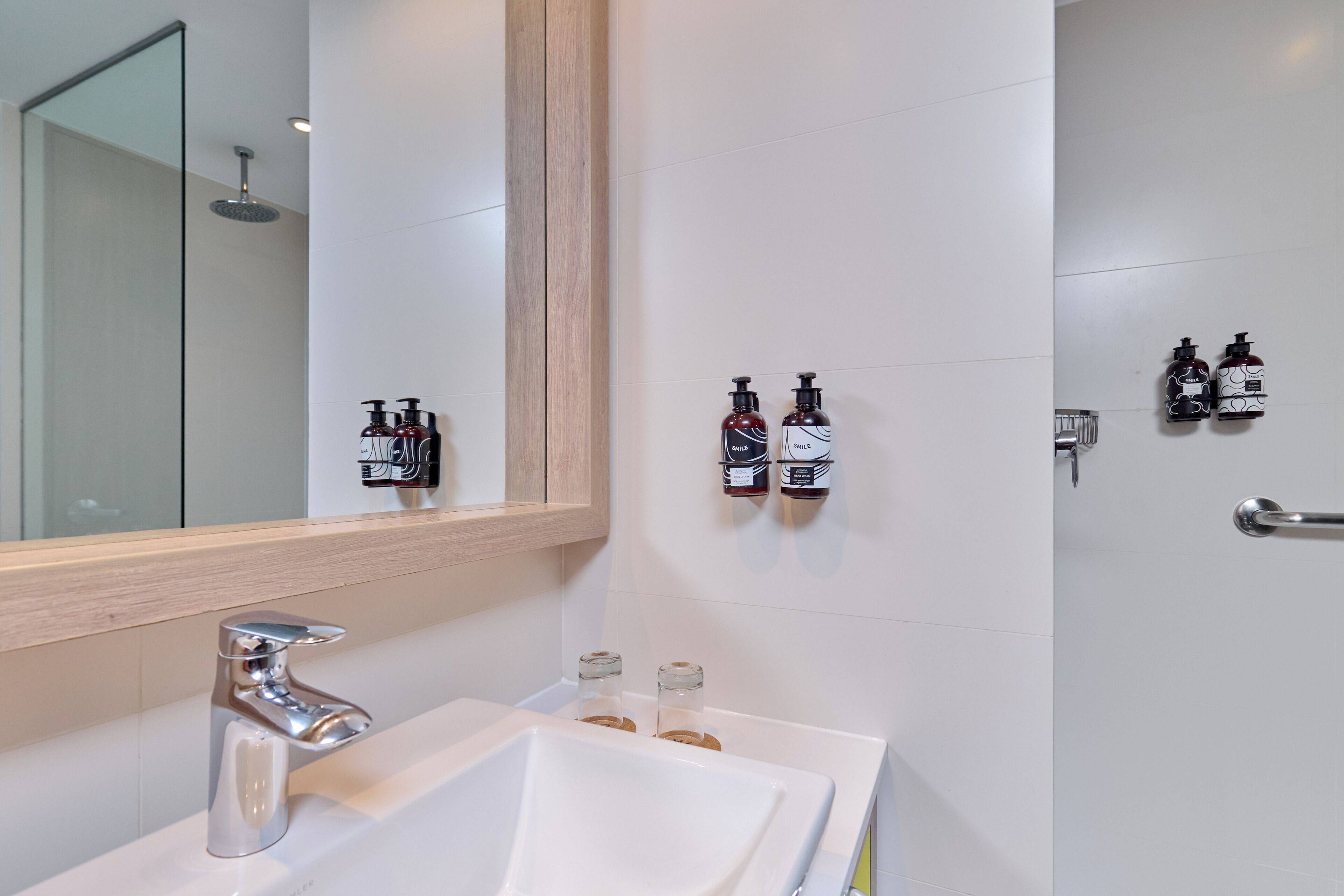 Un baño moderno con un lavabo blanco, grifo cromado y dos dispensadores de jabón para manos fijos en la pared.