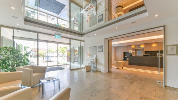 A spacious lobby with a reception desk, seating area, and a glass entrance leading outside.