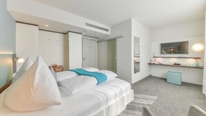 A modern hotel room with a bed, a small seating area, a kitchenette, and a bathroom.